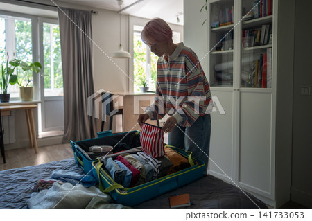 Organized mature woman traveler preparing for vacation trip and packing clothes in suitcase at home. Organized mature woman traveler preparing for vacation trip and packing clothes in suitcase at home. 141733053