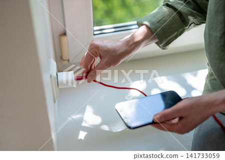 Woman connecting damaged phone charger cable trying to recharge smartphone plugging in outlet Woman connecting damaged phone charger cable trying to recharge smartphone plugging in outlet 141733059