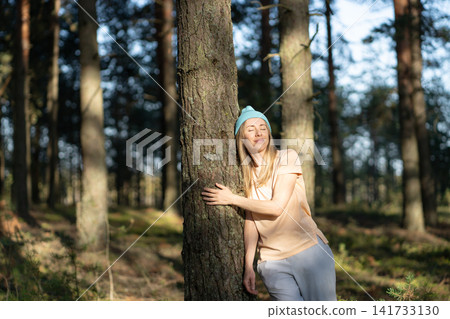 Carefree smiling woman hiking in forest alone, standing lean to tree enjoying peaceful moment. Carefree smiling woman hiking in forest alone, standing lean to tree enjoying peaceful moment. 141733130