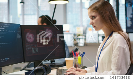 Female programmer in startup office struggling to fix application errors while coding. Young woman dealing with computer bugs while coding in software development agency, camera A 141733418
