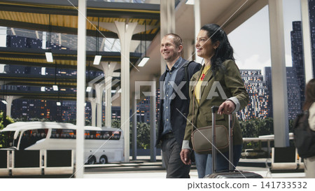 Smiling business travelers walk through coach station with trolley luggage, enjoying conversation. happy job colleagues moving together through modern bus terminal with baggage Smiling business travelers walk through coach station with trolley luggage, enjoying conversation. happy job colleagues moving together through modern bus terminal with baggage 141733532