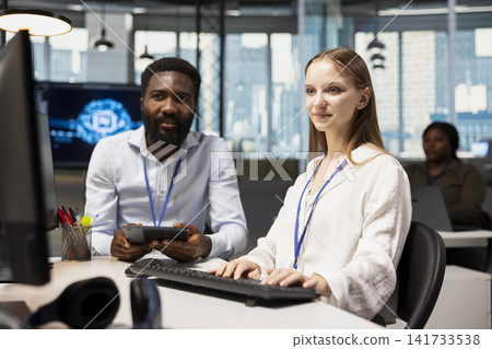 IT staff member helping female developer coding during internship in AI tech startup. Man providing support to new worker using computer in artificial intelligence agency IT staff member helping female developer coding during internship in AI tech startup. Man providing support to new worker using computer in artificial intelligence agency 141733538