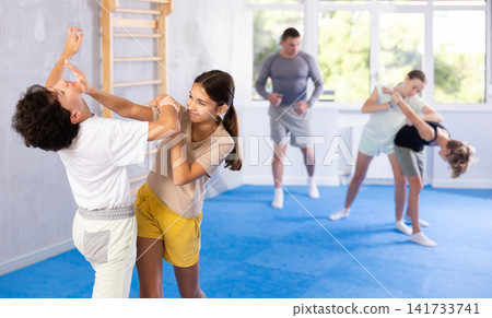 Group of children in sportswear exercising self protection techniques in pair during class at gym Group of children in sportswear exercising self protection techniques in pair during class at gym 141733741