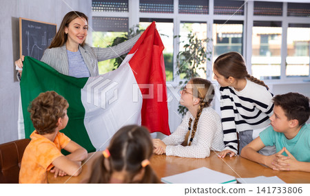 Teacher holds the flag of Italy in her hands and tells the students about country Teacher holds the flag of Italy in her hands and tells the students about country 141733806