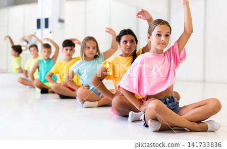 Children sitting and exercising ballet moves in studio Children sitting and exercising ballet moves in studio 141733836