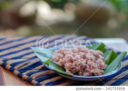 Traditional Indonesian brown rice served on banana leaf plate with natural lighting. Healthy Asian food, whole grain rice, authentic Southeast Asian cuisine. Traditional Indonesian brown rice served on banana leaf plate with natural lighting. Healthy Asian food, whole grain rice, authentic Southeast Asian cuisine. 141733916