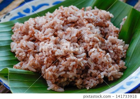 Close up of brown rice texture served on banana leaf. Healthy whole grain Asian food ingredient with natural daylight. Close up of brown rice texture served on banana leaf. Healthy whole grain Asian food ingredient with natural daylight. 141733918