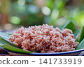 Traditional Indonesian brown rice served on banana leaf plate with natural lighting. Healthy Asian food, whole grain rice, authentic Southeast Asian cuisine. 141733919