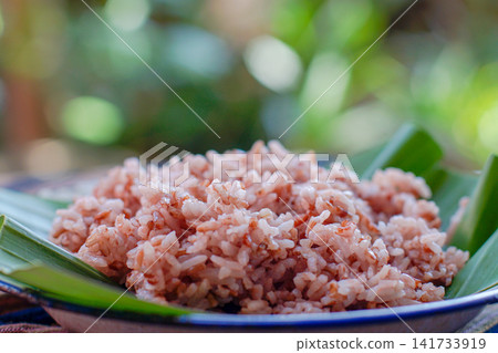 Traditional Indonesian brown rice served on banana leaf plate with natural lighting. Healthy Asian food, whole grain rice, authentic Southeast Asian cuisine. Traditional Indonesian brown rice served on banana leaf plate with natural lighting. Healthy Asian food, whole grain rice, authentic Southeast Asian cuisine. 141733919
