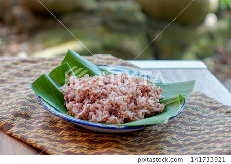 Traditional Indonesian brown rice served on banana leaf plate with natural lighting. Healthy Asian food, whole grain rice, authentic Southeast Asian cuisine. Traditional Indonesian brown rice served on banana leaf plate with natural lighting. Healthy Asian food, whole grain rice, authentic Southeast Asian cuisine. 141733921