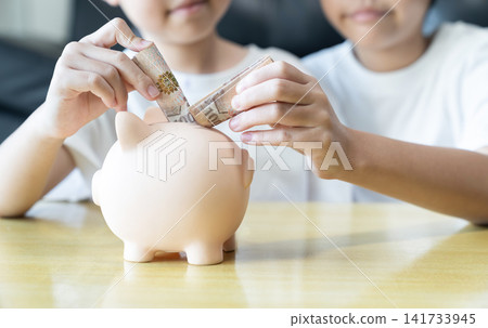 Children Hands placing banknotes into a piggy bank represents smart money management, financial planning, accumulated wealth, and long term economic security. Children Hands placing banknotes into a piggy bank represents smart money management, financial planning, accumulated wealth, and long term economic security. 141733945