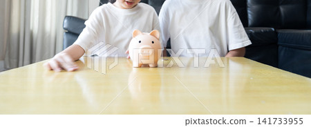 Two sister kids build healthy money habits through playful saving  future planning, wealth growth and financial literacy in front of black leather sofa at home. 141733955