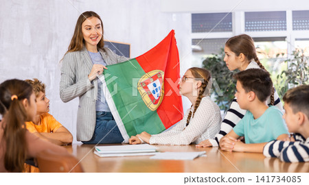 Group of curious preteen learners and young female teacher with flag of Portugal in schoolroom of academy Group of curious preteen learners and young female teacher with flag of Portugal in schoolroom of academy 141734085