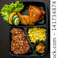 Top view of a roasted chicken leg bento meal served with rice, eggs and vegetables in a compartmented takeaway box. Balanced protein food concept. 141734874