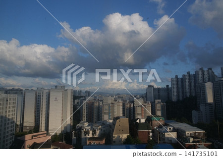 Urban apartment complex under a blue sky and fluffy white clouds Urban apartment complex under a blue sky and fluffy white clouds 141735101