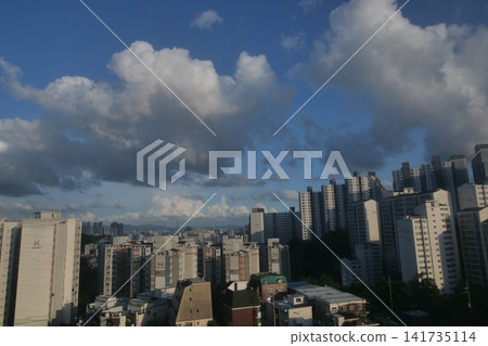 Urban apartment complex under a blue sky and fluffy white clouds Urban apartment complex under a blue sky and fluffy white clouds 141735114