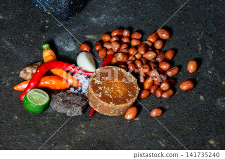 Top view of traditional Indonesian sambal ingredients on a stone mortar with chili peppers, peanuts, palm sugar, garlic, salt, shrimp paste, and lime. Top view of traditional Indonesian sambal ingredients on a stone mortar with chili peppers, peanuts, palm sugar, garlic, salt, shrimp paste, and lime. 141735240