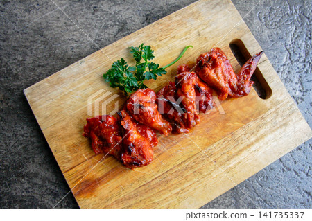 Top view of spicy chicken wings with hot sauce on wooden board and copy space. Suitable for restaurant menus, BBQ promotions and food advertising layouts. Top view of spicy chicken wings with hot sauce on wooden board and copy space. Suitable for restaurant menus, BBQ promotions and food advertising layouts. 141735337