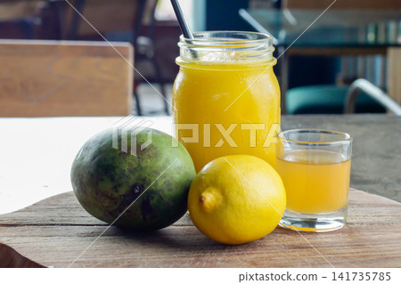 Mango juice with fresh mango and lemon served on a rustic wooden board in a casual cafe, showing a bright tropical beverage concept with natural fruit ingredients and copy space. Mango juice with fresh mango and lemon served on a rustic wooden board in a casual cafe, showing a bright tropical beverage concept with natural fruit ingredients and copy space. 141735785