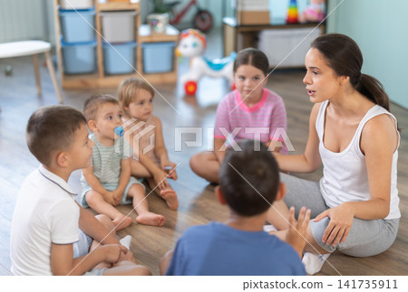 Kindergarten teacher reading to children in kindergarten. Children listen attentively to lessons, engaged in learning activities together Kindergarten teacher reading to children in kindergarten. Children listen attentively to lessons, engaged in learning activities together 141735911