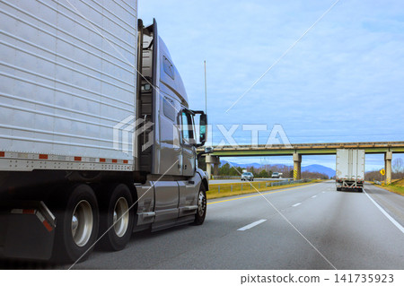 Two trucks drive on highway with grass trees nearby bridge is visible in South Carolina Two trucks drive on highway with grass trees nearby bridge is visible in South Carolina 141735923