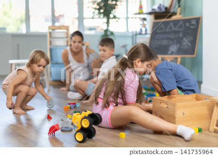 Group of children sitting on floor and playing with cubes and cars in childcare center Group of children sitting on floor and playing with cubes and cars in childcare center 141735964