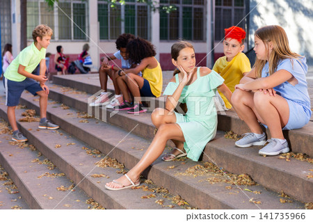 Happy tweenagers friends sitting on steps outdoors and chatting Happy tweenagers friends sitting on steps outdoors and chatting 141735966