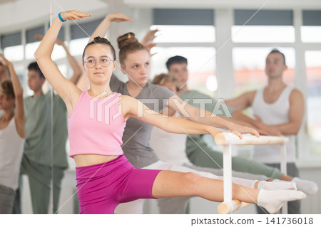 Teen ballet students prepare for classes, near ballet bare stretch legs under man teacher guidance Teen ballet students prepare for classes, near ballet bare stretch legs under man teacher guidance 141736018