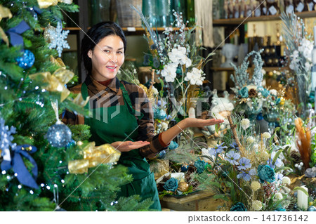 Woman salesman decorates christmas tree in flower shop 141736142