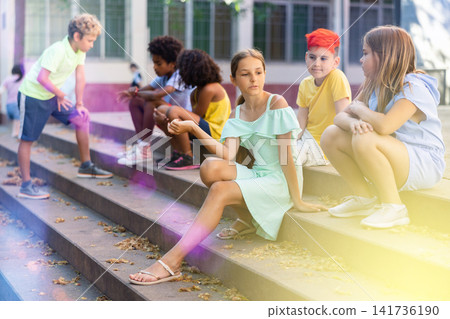 Children talking together while sitting on stairs outdoors Children talking together while sitting on stairs outdoors 141736190