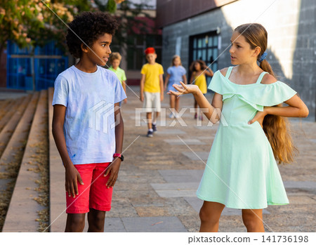Preteen girl talking friendly with african friend while walking Preteen girl talking friendly with african friend while walking 141736198