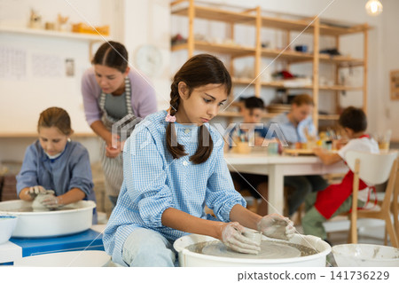 Girl working at a potter's wheel with clay Girl working at a potter's wheel with clay 141736229