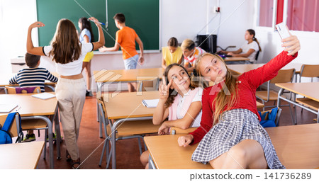 Two cheerful schoolgirls take a selfie during recess in classroom Two cheerful schoolgirls take a selfie during recess in classroom 141736289