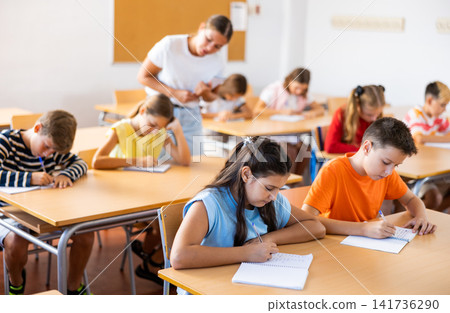 School kids with pens and notebooks studying in classroom with teacher School kids with pens and notebooks studying in classroom with teacher 141736290