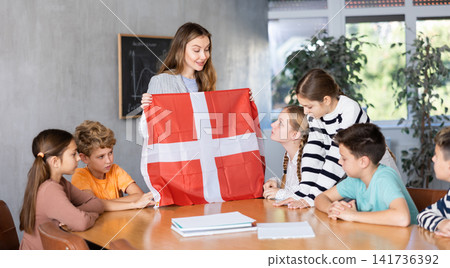 Teacher showing Denmark flag to group of preteen schoolchildren 141736392