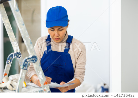 Woman worker filling documents during repair works indoors Woman worker filling documents during repair works indoors 141736452