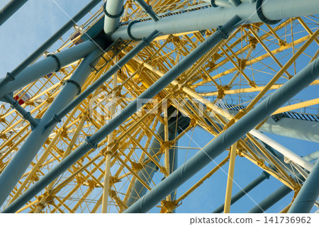 Structural elements of ferris wheel create an intricate pattern against blue sky Structural elements of ferris wheel create an intricate pattern against blue sky 141736962