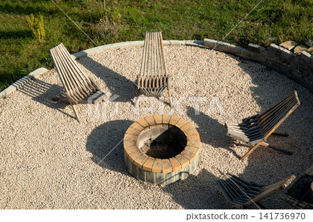 Chairs arranged around a circular fire pit in a tranquil garden Chairs arranged around a circular fire pit in a tranquil garden 141736970