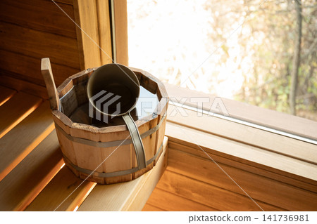 Bucket with ladle sits in serene sauna environment. Relaxation and wellness concept Bucket with ladle sits in serene sauna environment. Relaxation and wellness concept 141736981