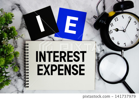 IE Interest Expense text written on notepad with alarm clock and magnifying glass on marble background IE Interest Expense text written on notepad with alarm clock and magnifying glass on marble background 141737979