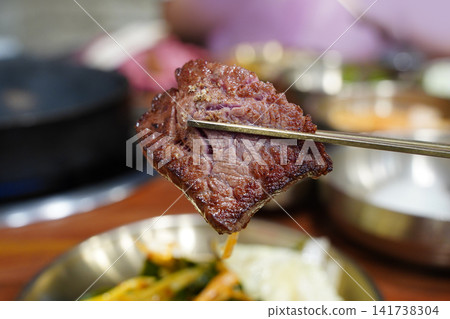 Holding a piece of juicy grilled Korean beef Hanwoo with chopsticks close up Holding a piece of juicy grilled Korean beef Hanwoo with chopsticks close up 141738304