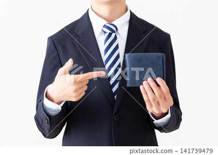 A young businessman in a suit points to a navy blue wallet. A young businessman in a suit points to a navy blue wallet. 141739479