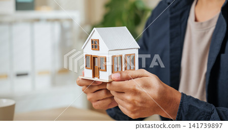 Real estate agent holds a miniature house model, representing property, finance, home loans, and housing concepts Real estate agent holds a miniature house model, representing property, finance, home loans, and housing concepts 141739897