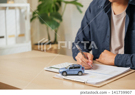 A man writes his signature on a car finance or lease agreement. Great for vehicle buying, renting, or dealership deals emphasizing auto loans A man writes his signature on a car finance or lease agreement. Great for vehicle buying, renting, or dealership deals emphasizing auto loans 141739907