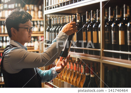 Professional Sommelier Examining Selection of Wine Bottles in Cellar 141740464