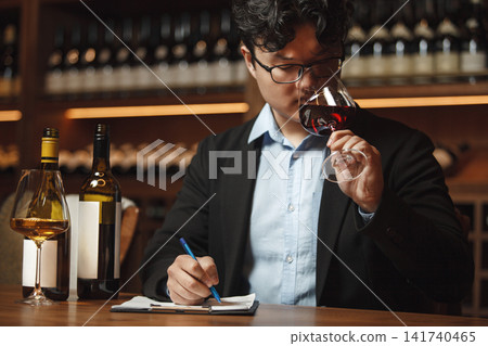 Sommelier Writing Notes With Glass of Wine Sitting at Table Being in Cellar Sommelier Writing Notes With Glass of Wine Sitting at Table Being in Cellar 141740465