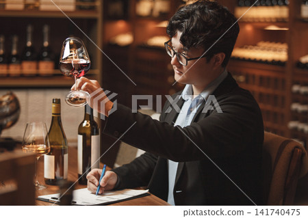 Professional Sommelier Conducts Wine Tasting Session Sitting at Table in Cellar.  141740475
