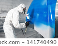 Worker in protective mask and jumpsuit overall spraying base coat of paint on car body elements in painted chamber using professional airbrush. 141740490