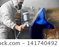 Automobile repairman painter in mask and protective workwear painting car body in paint chamber. 141740492