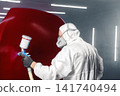 Automobile repairman painter in protective workwear and respirator paints part of car body in paint chamber using airbrush, close up. Restoration painting of car in the paint chamber service.  141740494